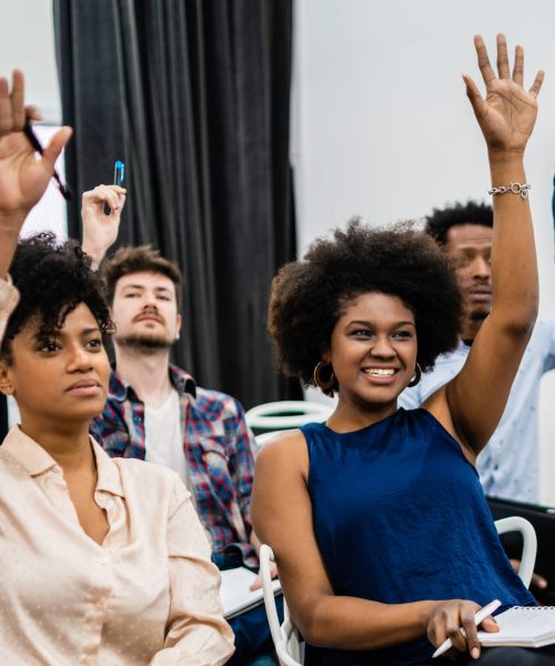 Group of young people sitting on conference together while raising their hands to ask a question. Business team meeting seminar training concept.